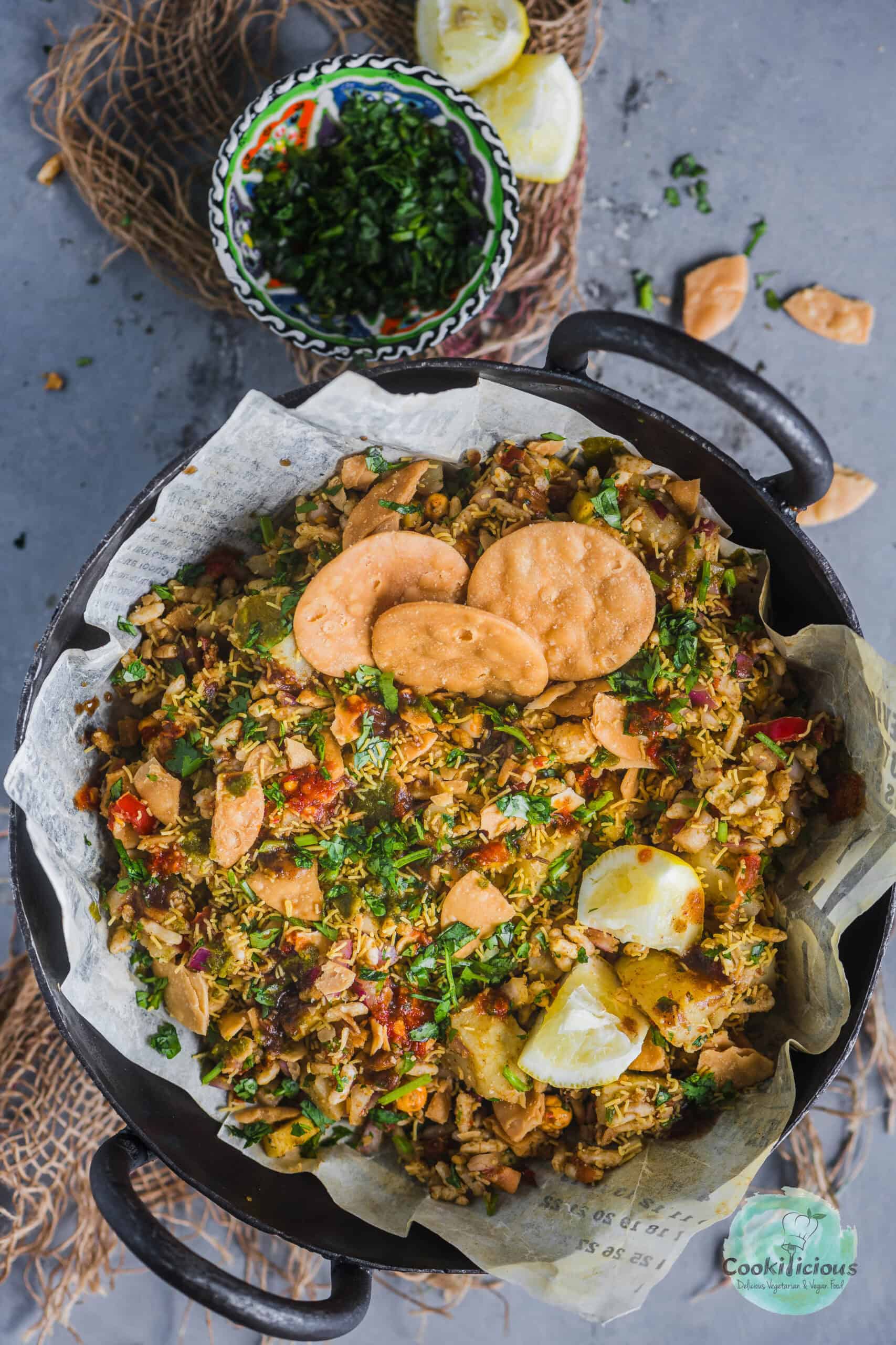 Bhel Puri served in a round bowl with papdi on top.