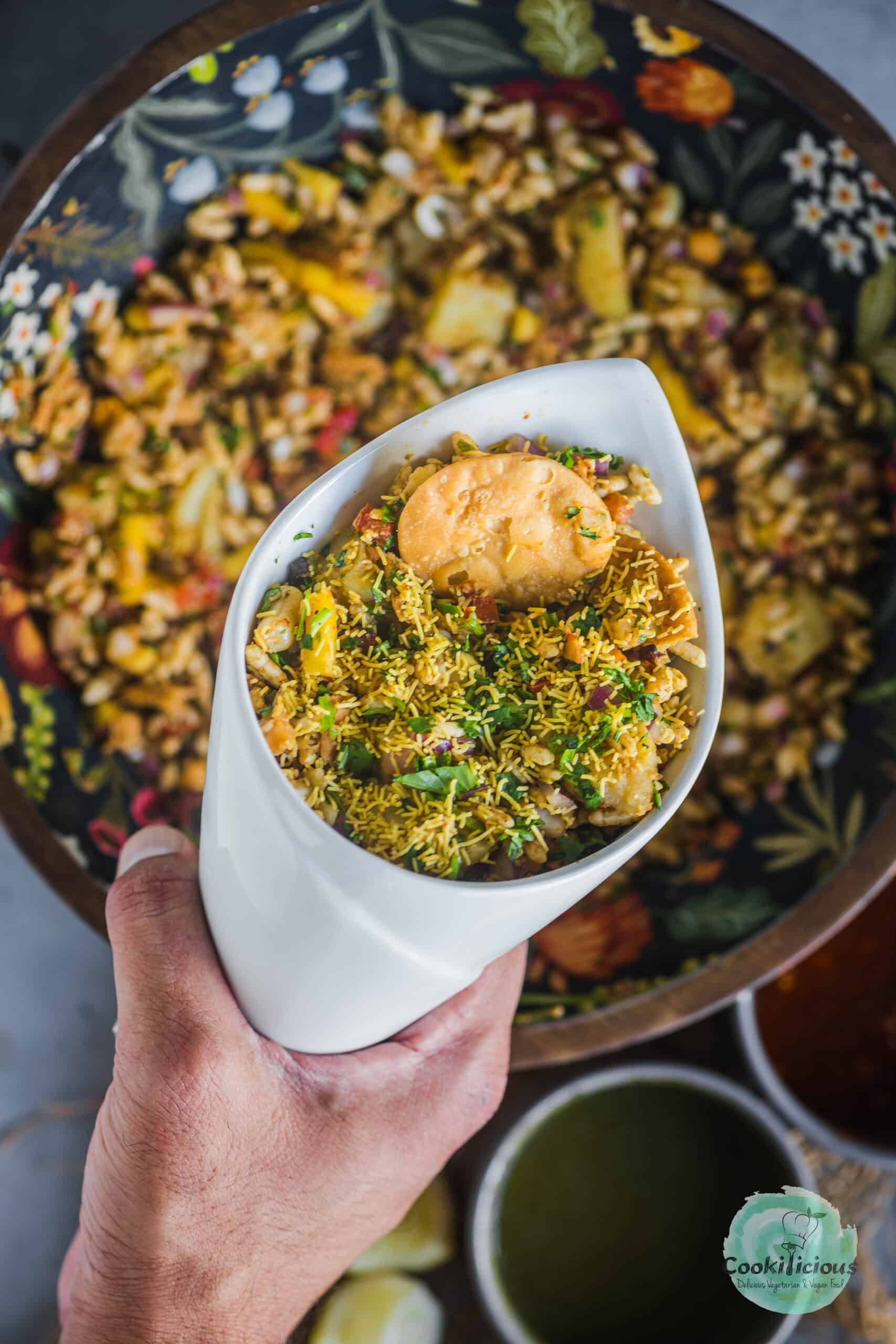 a hand holding a cone filled with Bombay Bhel.