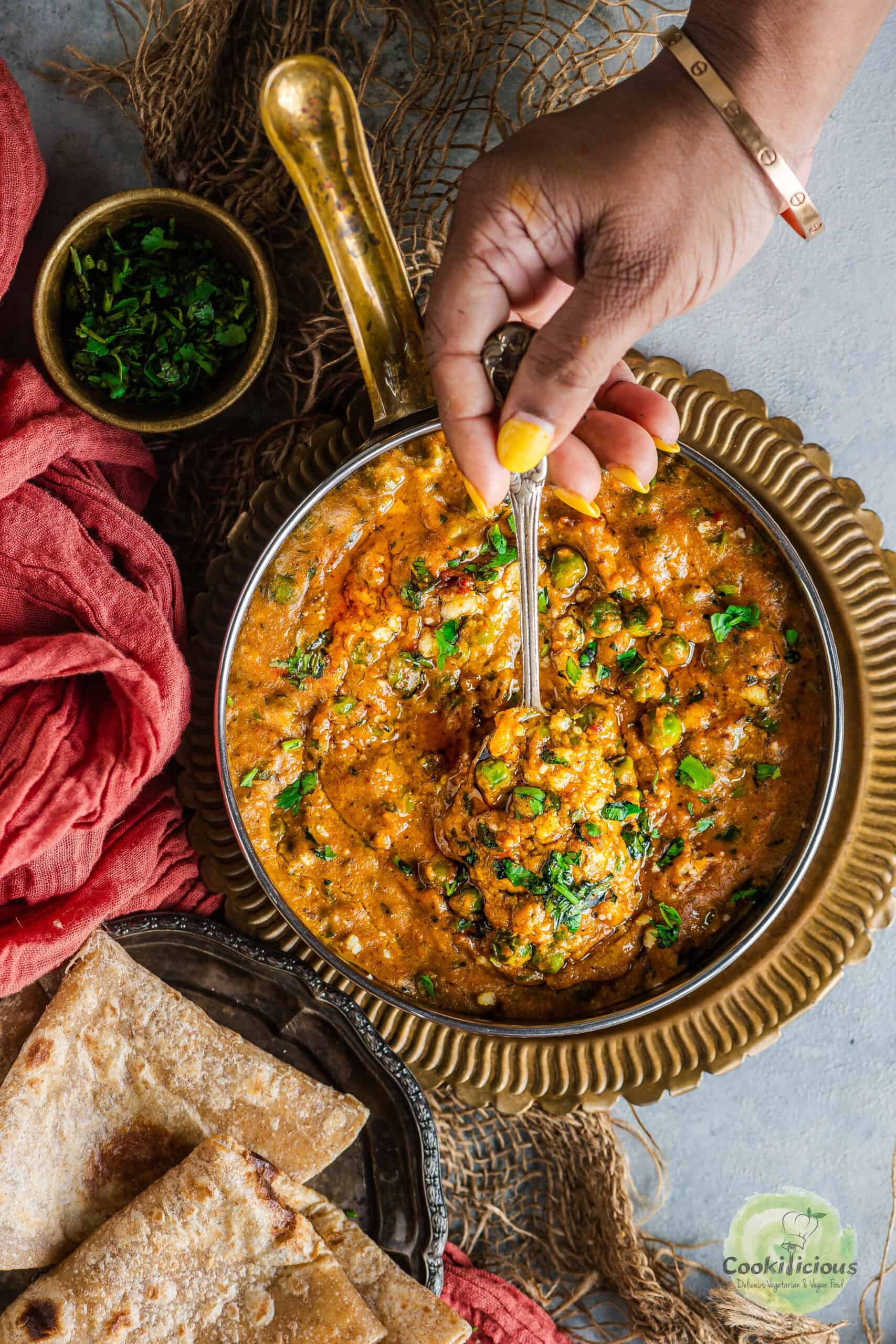 A hand digging into a bowl of Khoya Mutter with a spoon.