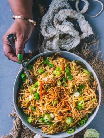 A hand holding a fork and digging into a bowl of Veg Hakka Noodles.