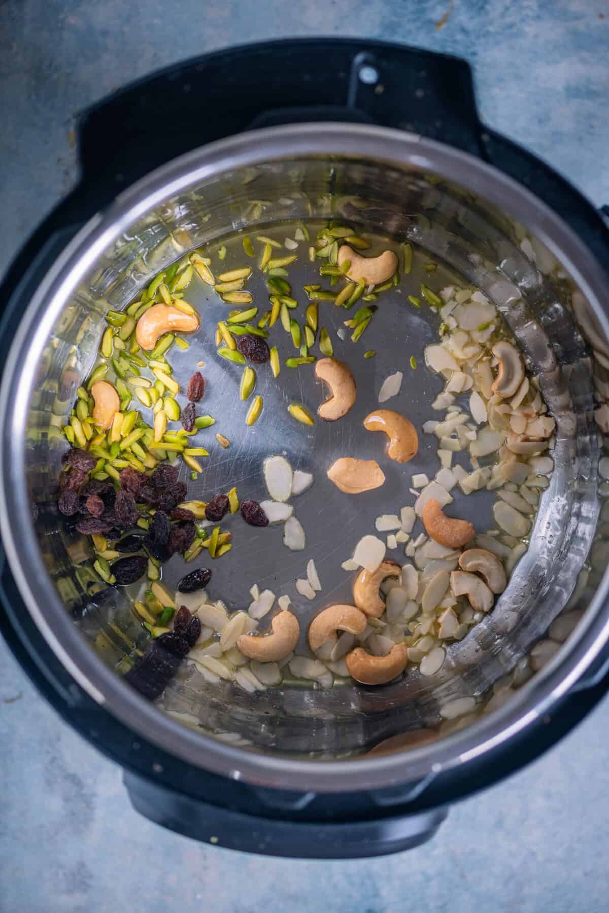 Cashews, almonds, pistachios, and raisins sautéing in ghee in an Instant Pot.