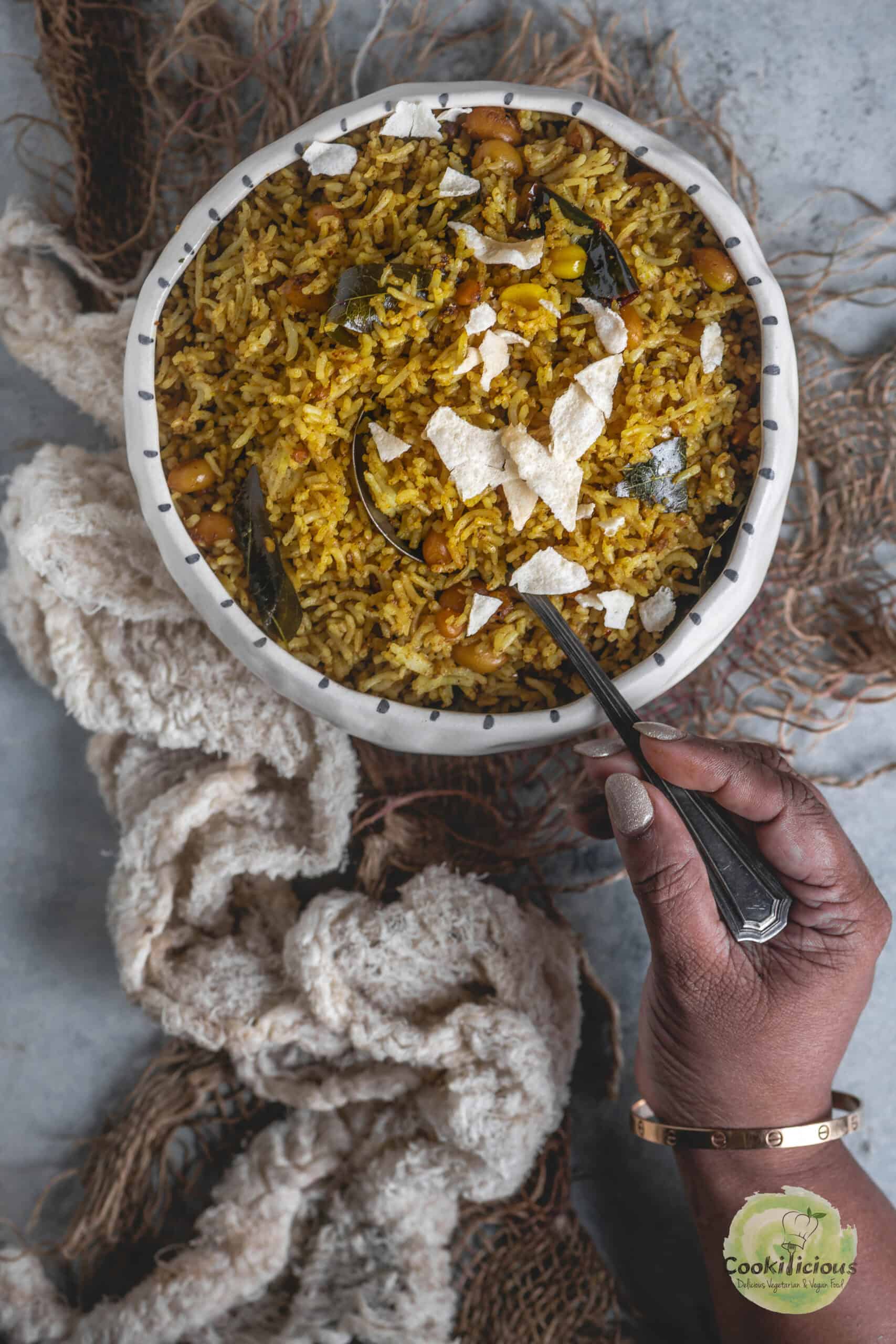 A hand digging into a bowl of Tamarind rice with a spoon.