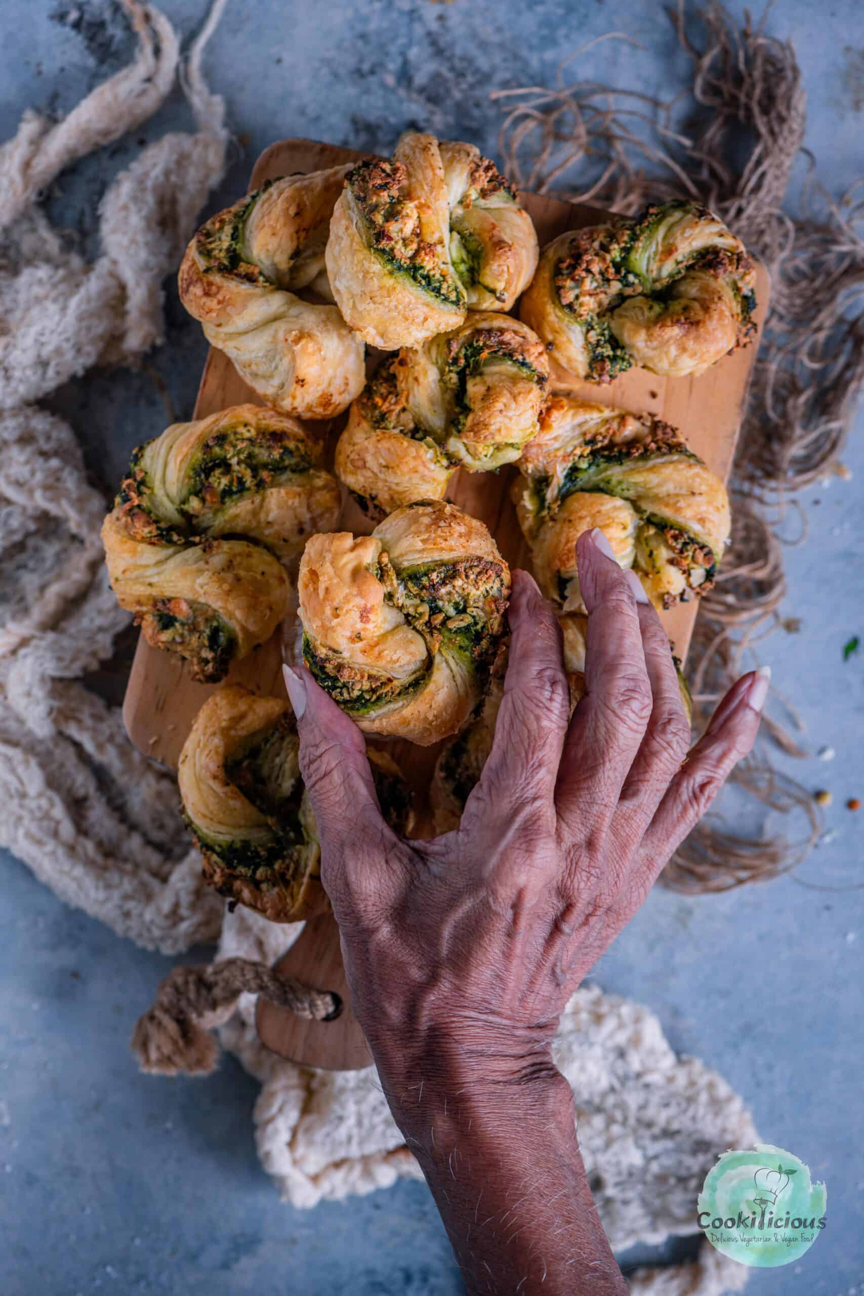 A hand picking one Palak Paneer Puff from a platter.