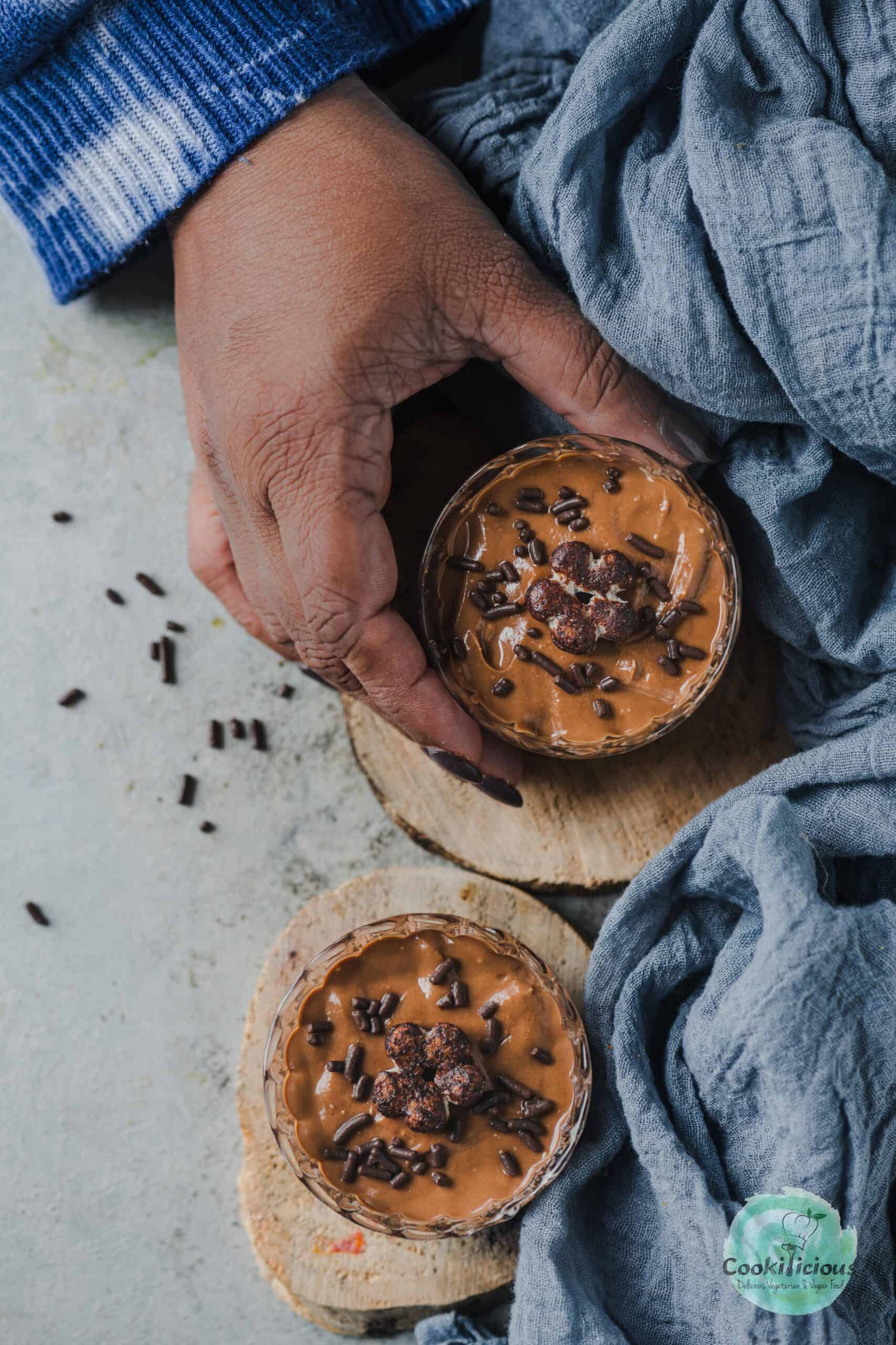 2 jars of homemade chocolate ricotta mousse where one hand in holding one of the jars.