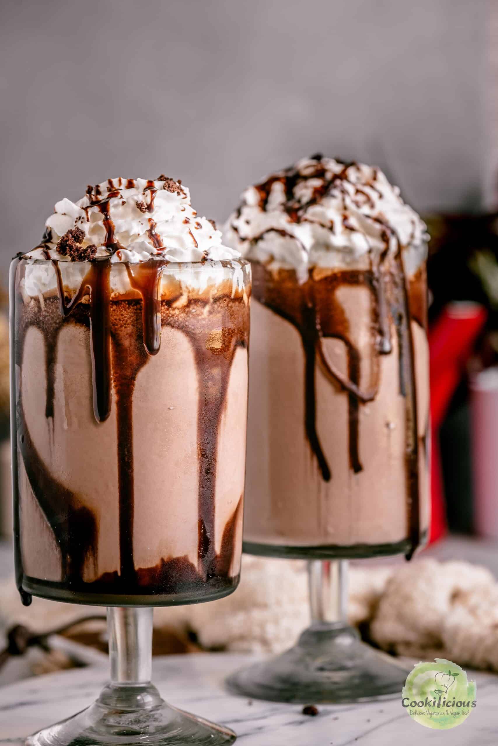 Two tall glasses of rich, creamy chocolate brownie milkshake topped with whipped cream, brownie crumbles, and chocolate drizzle.