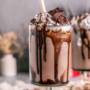 A single tall glass of brownie milkshake served with a straw and garnished with a fudgy brownie wedge.