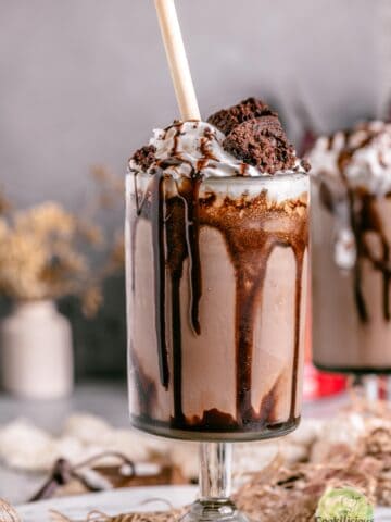 A single tall glass of brownie milkshake served with a straw and garnished with a fudgy brownie wedge.