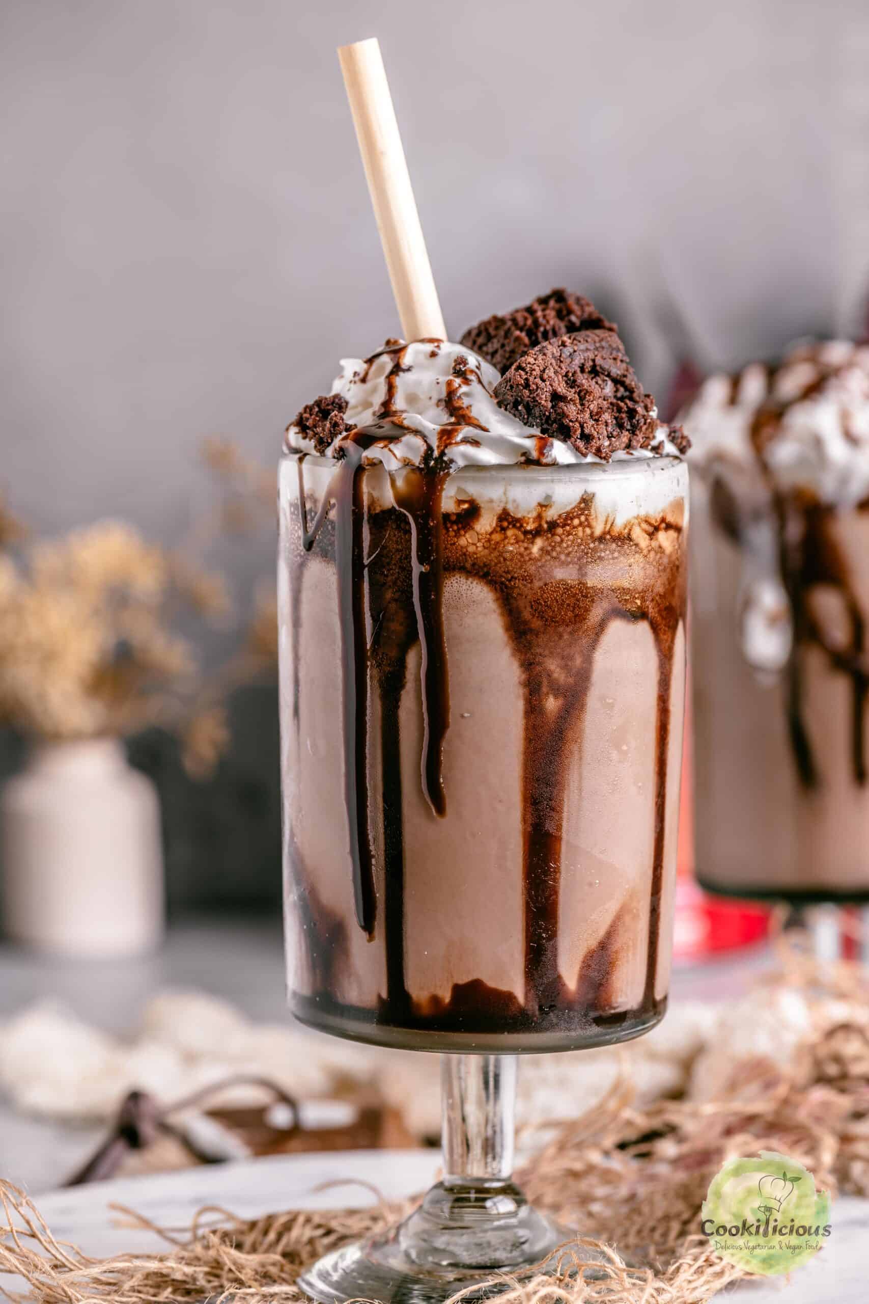 A single tall glass of brownie milkshake served with a straw and garnished with a fudgy brownie wedge.