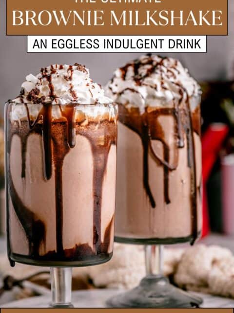 Two tall glasses of rich, creamy chocolate brownie milkshake topped with whipped cream, brownie crumbles, and chocolate drizzle and text at the top and bottom.