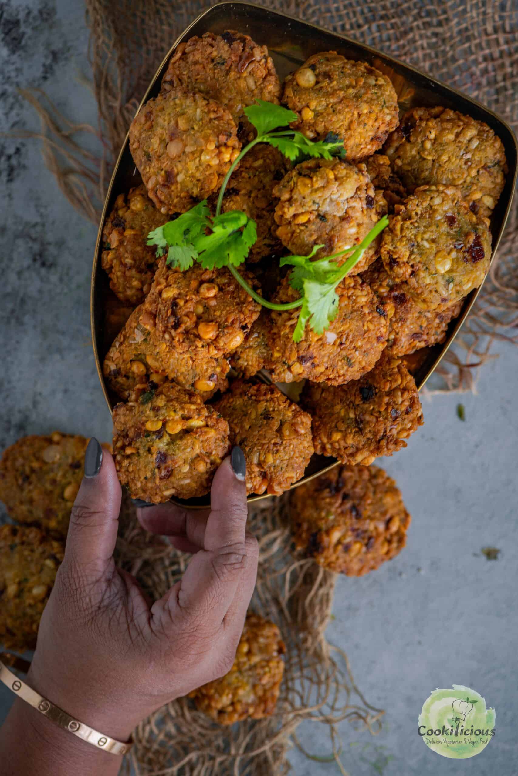 A rustic display of dal vadas served on a platter and a hand picking one up.