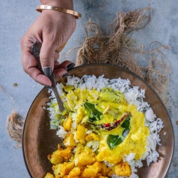 Mor Kuzhambu served with rice and potato Fry in a bowl and a hand digging into it with a spoon.