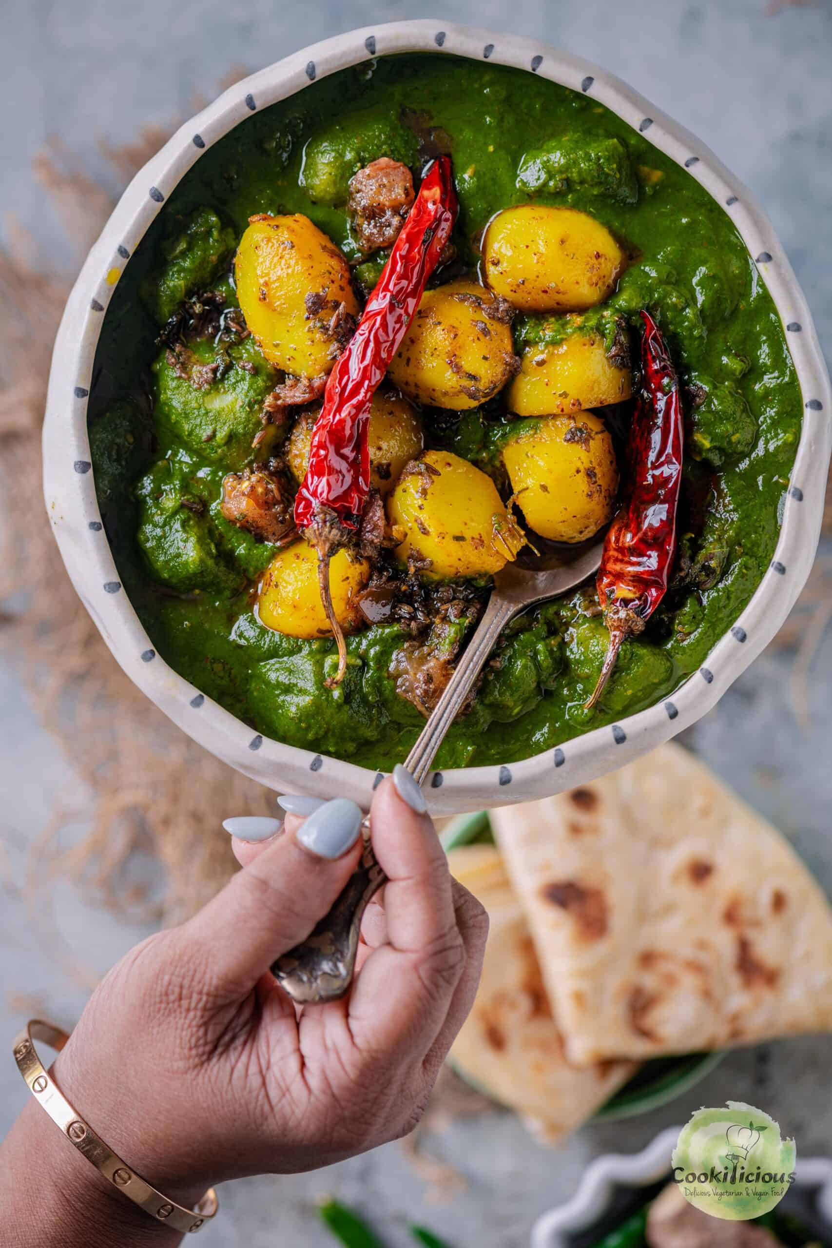 a hand digging into a bowl of Aloo Palak with a spoon.