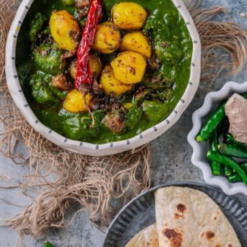 A bowl of Aloo Palak curry with golden potatoes in a creamy spinach gravy, served with chapati on the side.