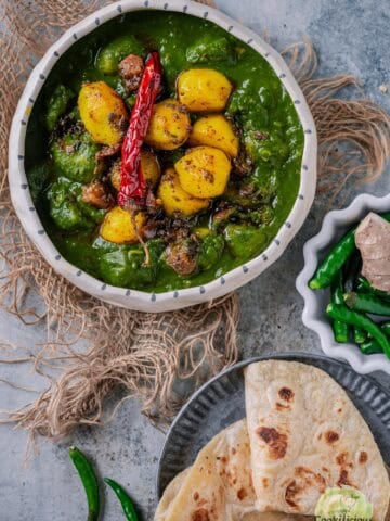 A bowl of Aloo Palak curry with golden potatoes in a creamy spinach gravy, served with chapati on the side.