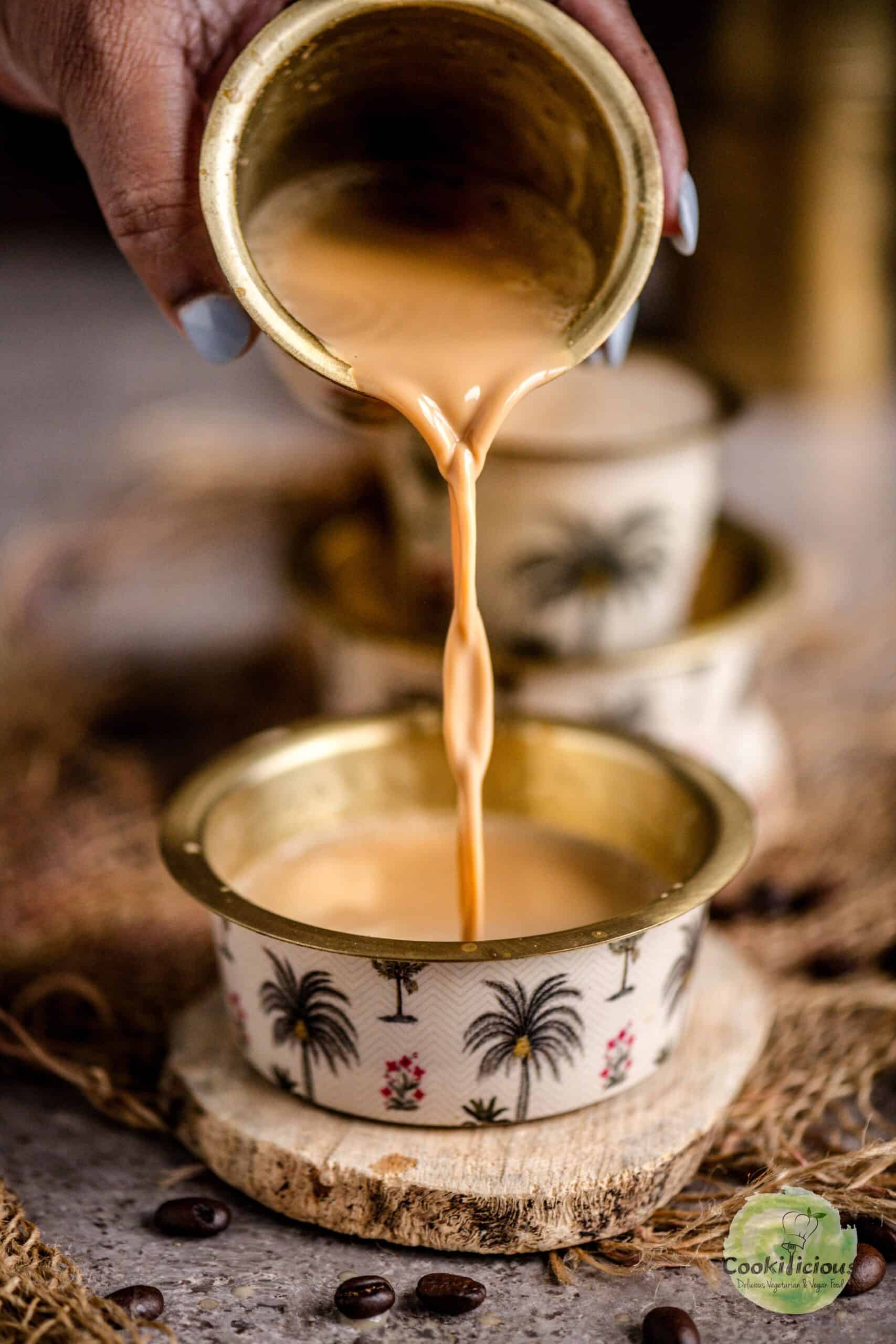 A hand pouring South Indian Filter Coffee from a metal glass into the davara.