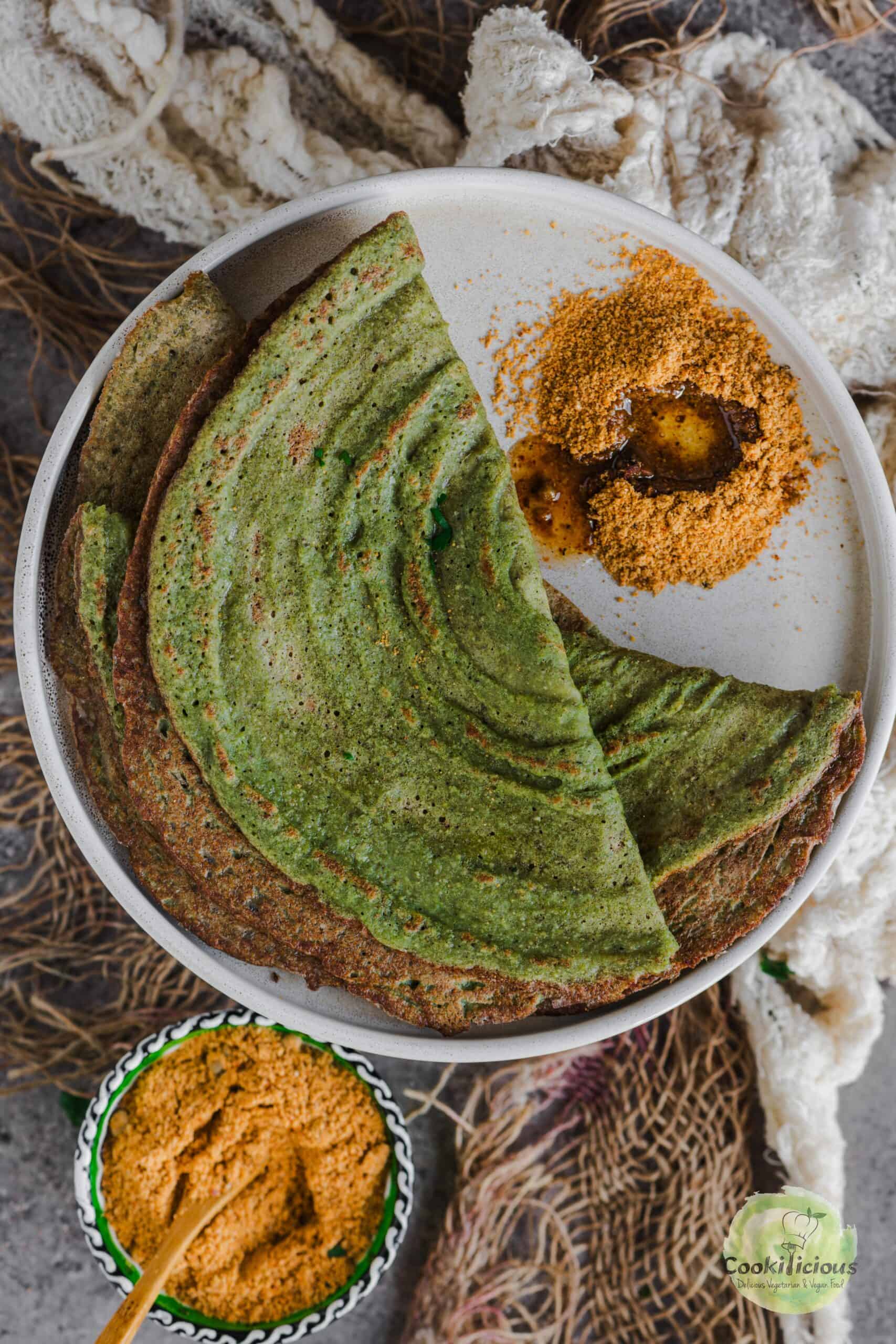 A golden-brown, crispy pesarattu served on a white plate with a side of mulagapodi.