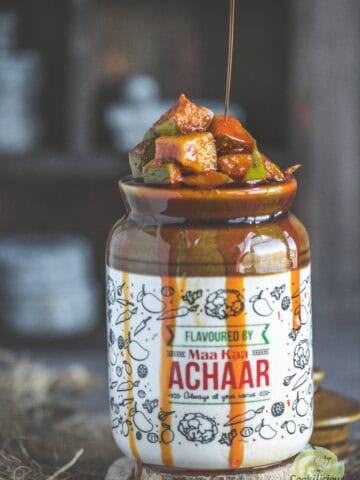 Close-up of tangy South Indian Manga Urugai served in a ceramic jar with gingelly oil being poured over it.