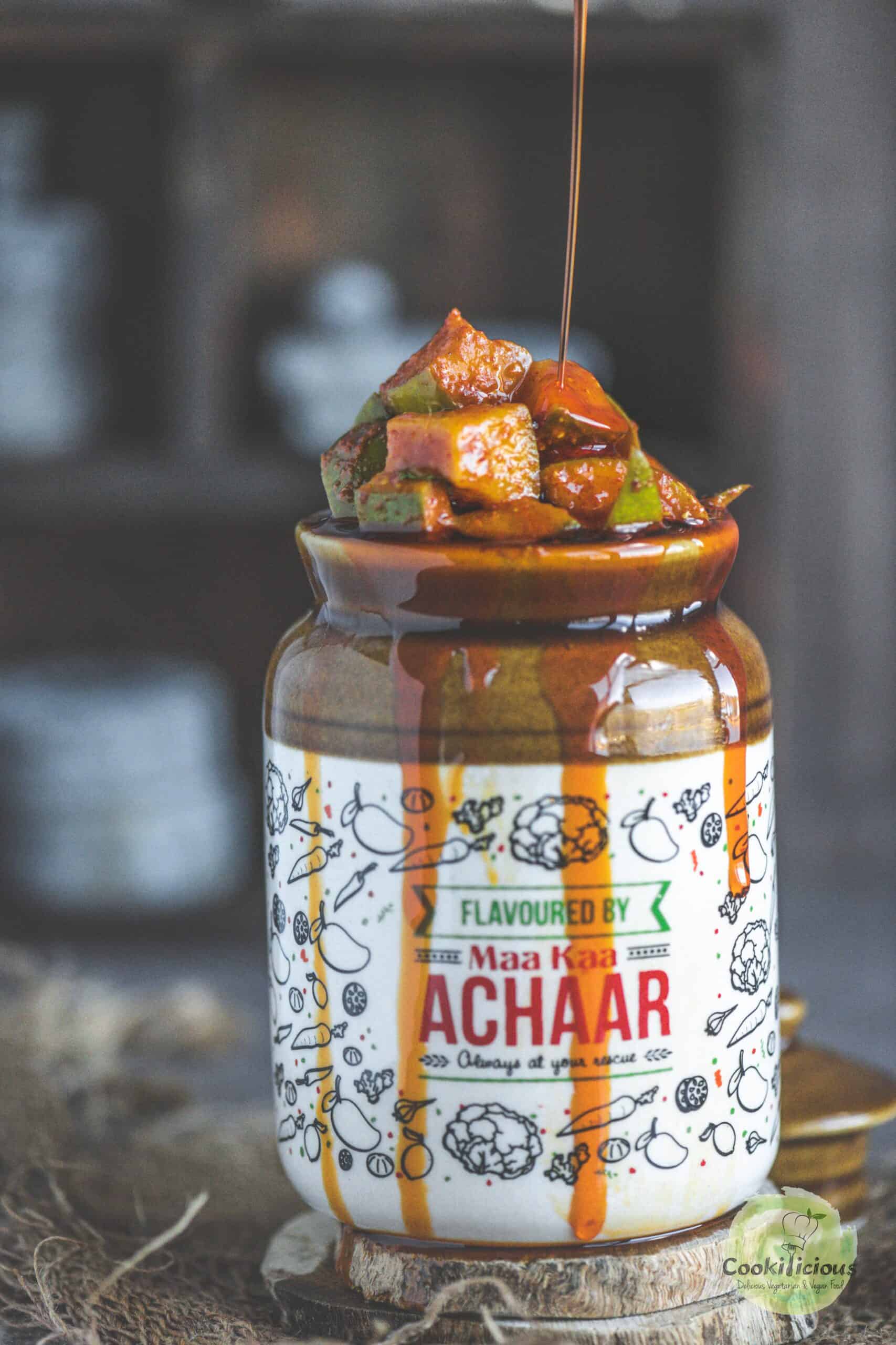 Close-up of tangy South Indian Manga Urugai served in a ceramic jar with gingelly oil being poured over it.
