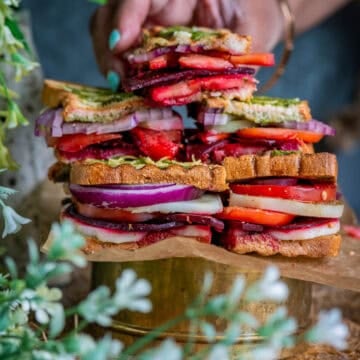 Stack of Bombay vegetable Sandwiches and one hand picking one up.
