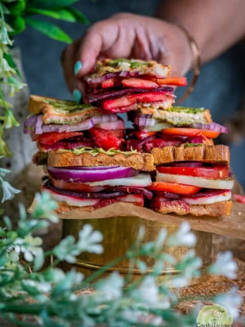 Stack of Bombay vegetable Sandwiches and one hand picking one up.