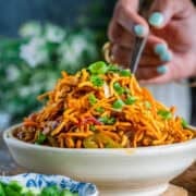 A hand digging into a bowl of freshly made Chinese Bhel holding a fork.