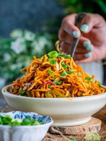 A hand digging into a bowl of freshly made Chinese Bhel holding a fork.