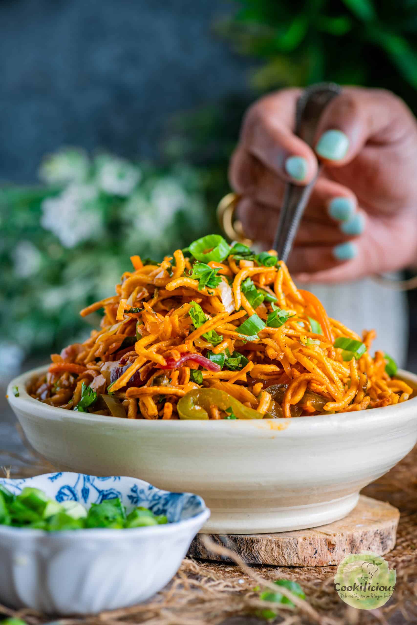 A hand digging into a bowl of freshly made Chinese Bhel holding a fork.