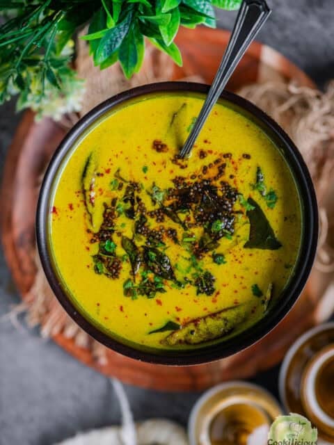 yellow Gujarati Kadhi made with besan and dahi served in a bowl with tadka on top.