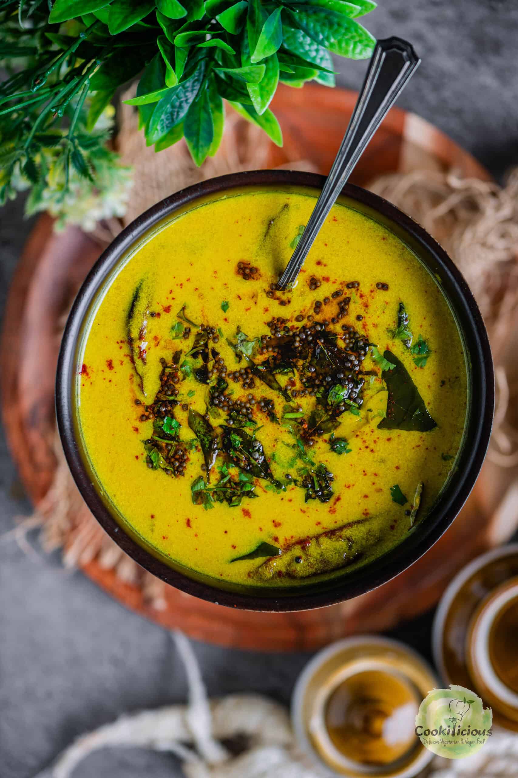 yellow Gujarati Kadhi made with besan and dahi served in a bowl with tadka on top.