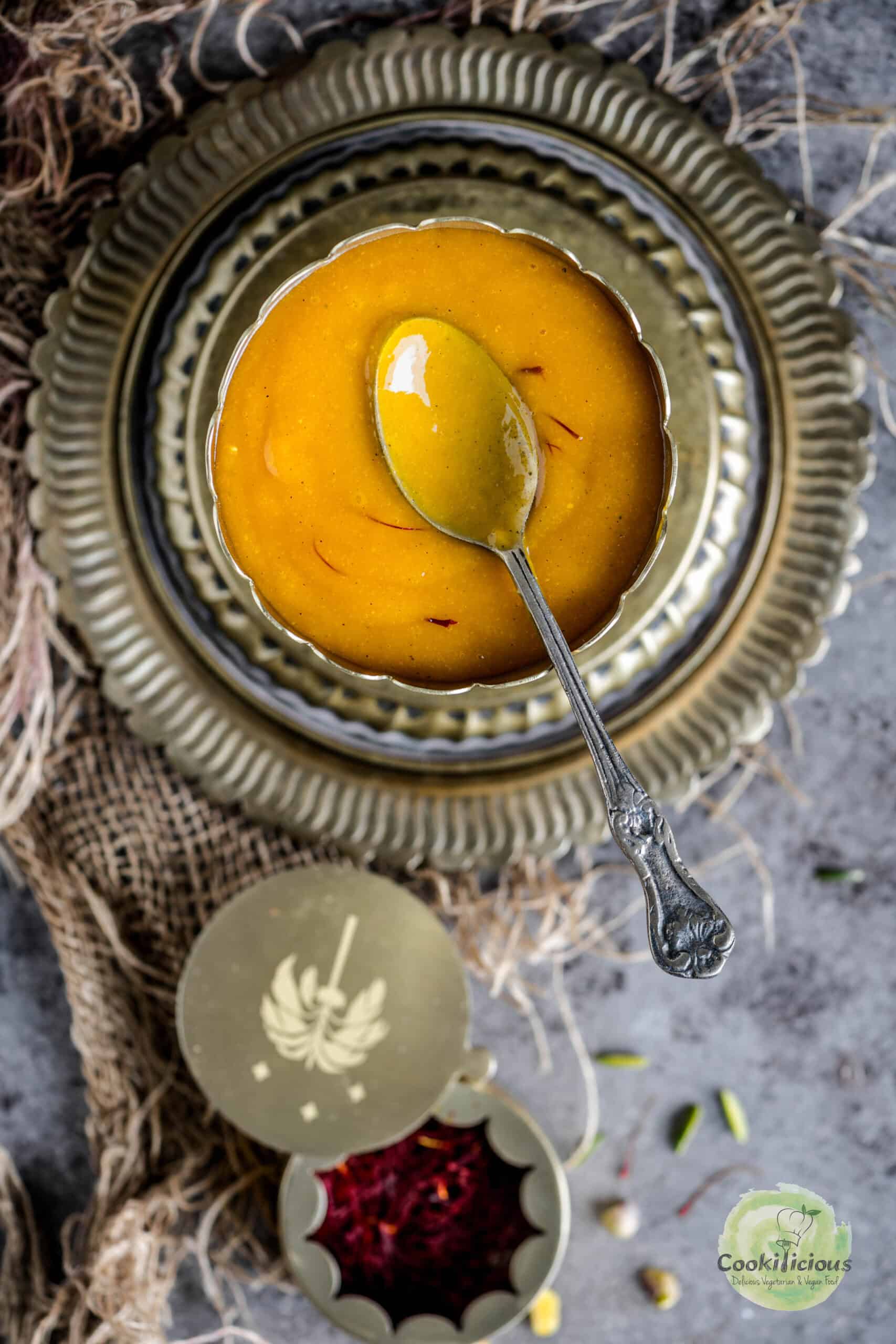 Aamras served in a brass bowl and spoon in it.