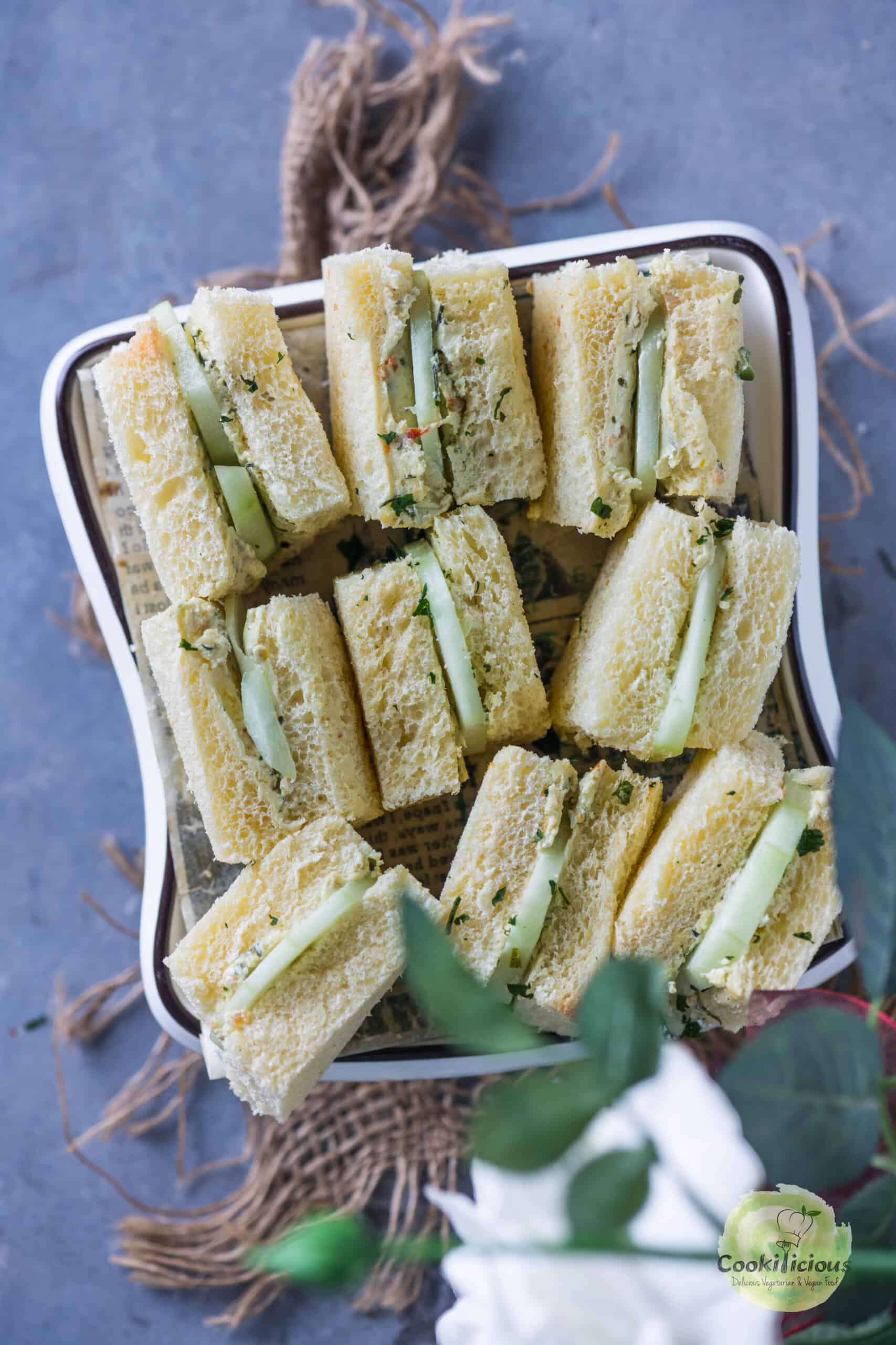 Stacked cucumber and cream cheese sandwiches served on a white plate.