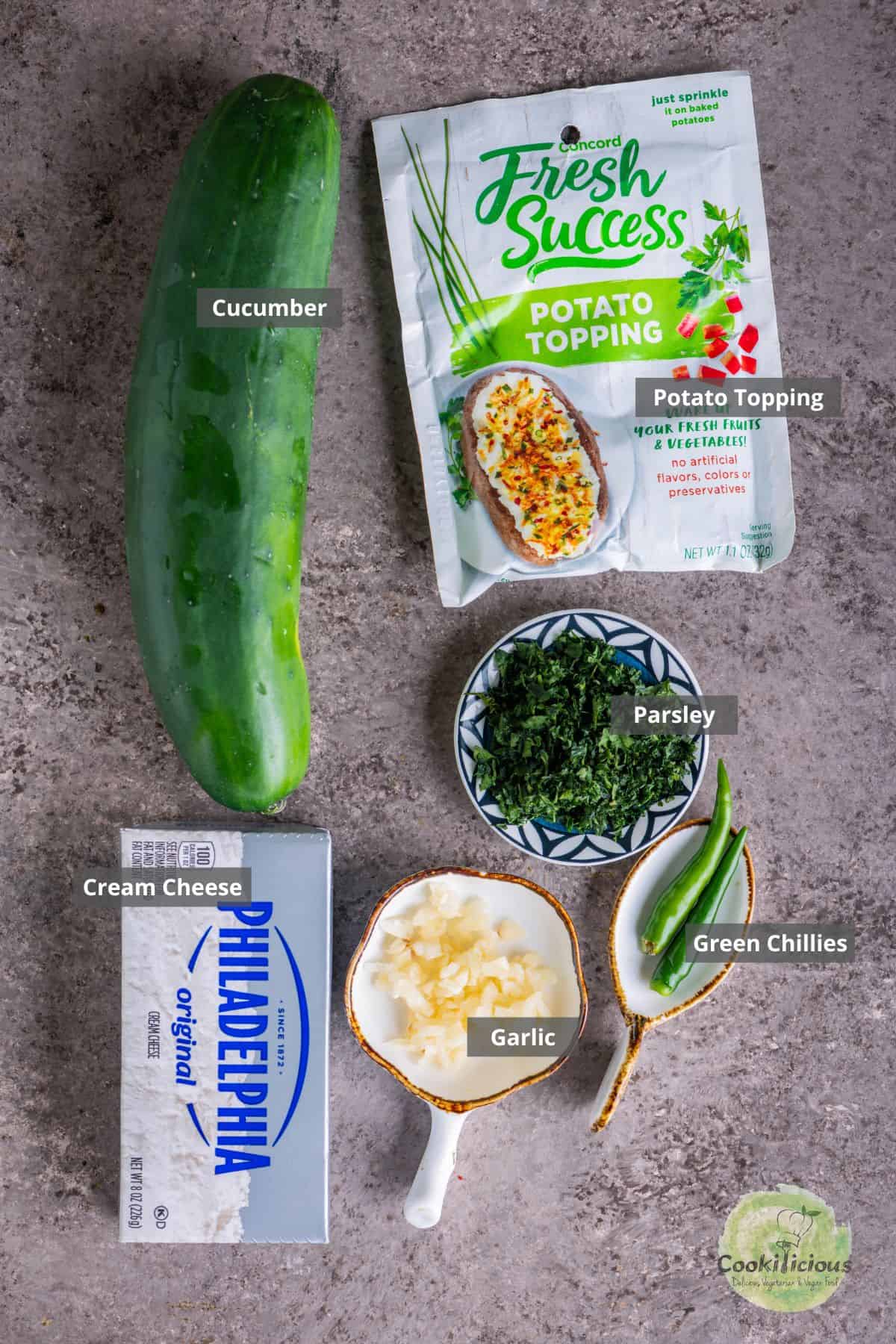 Ingredients for cucumber and cream cheese sandwiches – cucumbers, bread, herbs, and cream cheese arranged on a table with labels on them.