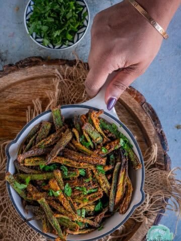 A hand holding a air fried Kurkuri Bhindi platter.