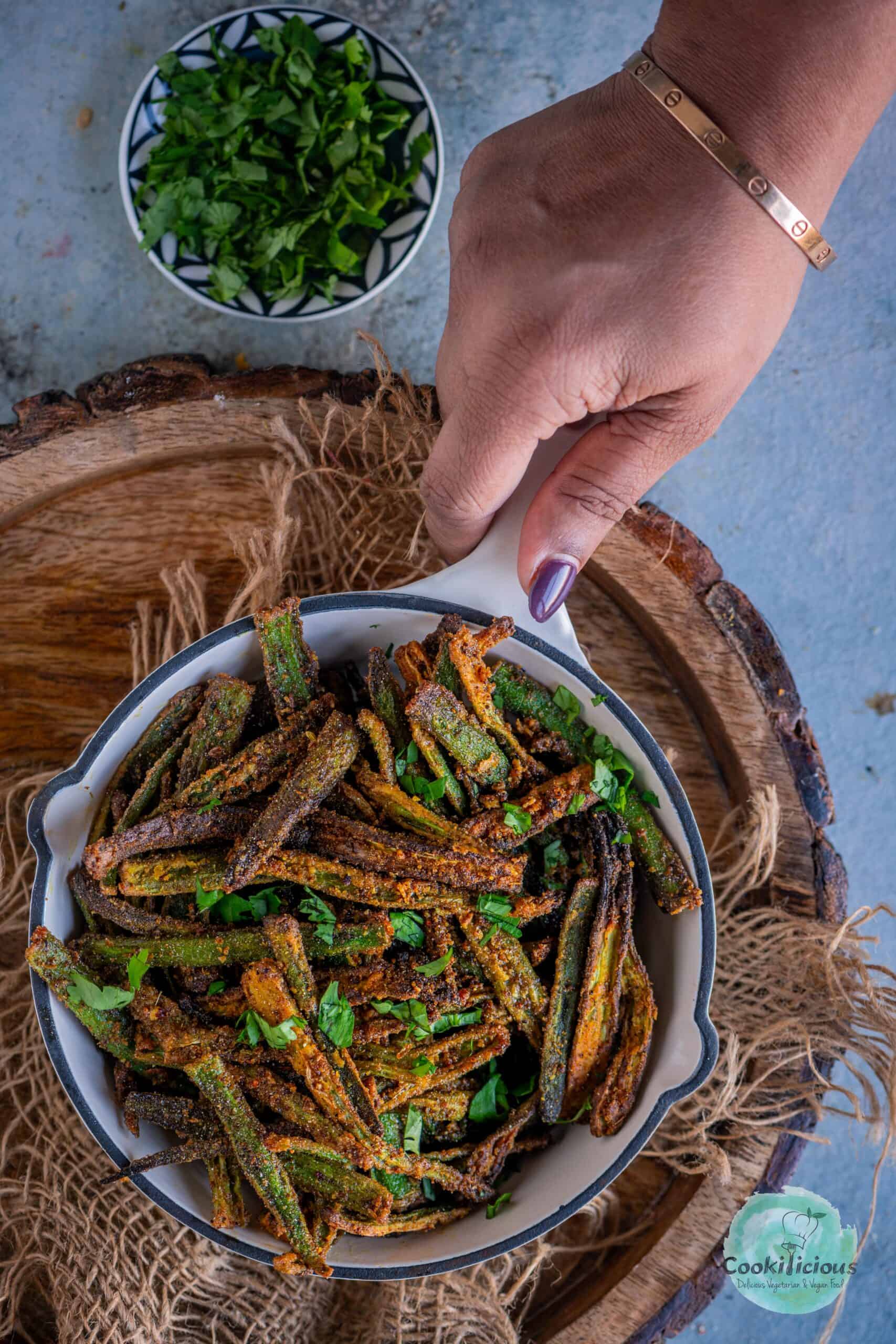 A hand holding a air fried Kurkuri Bhindi platter.