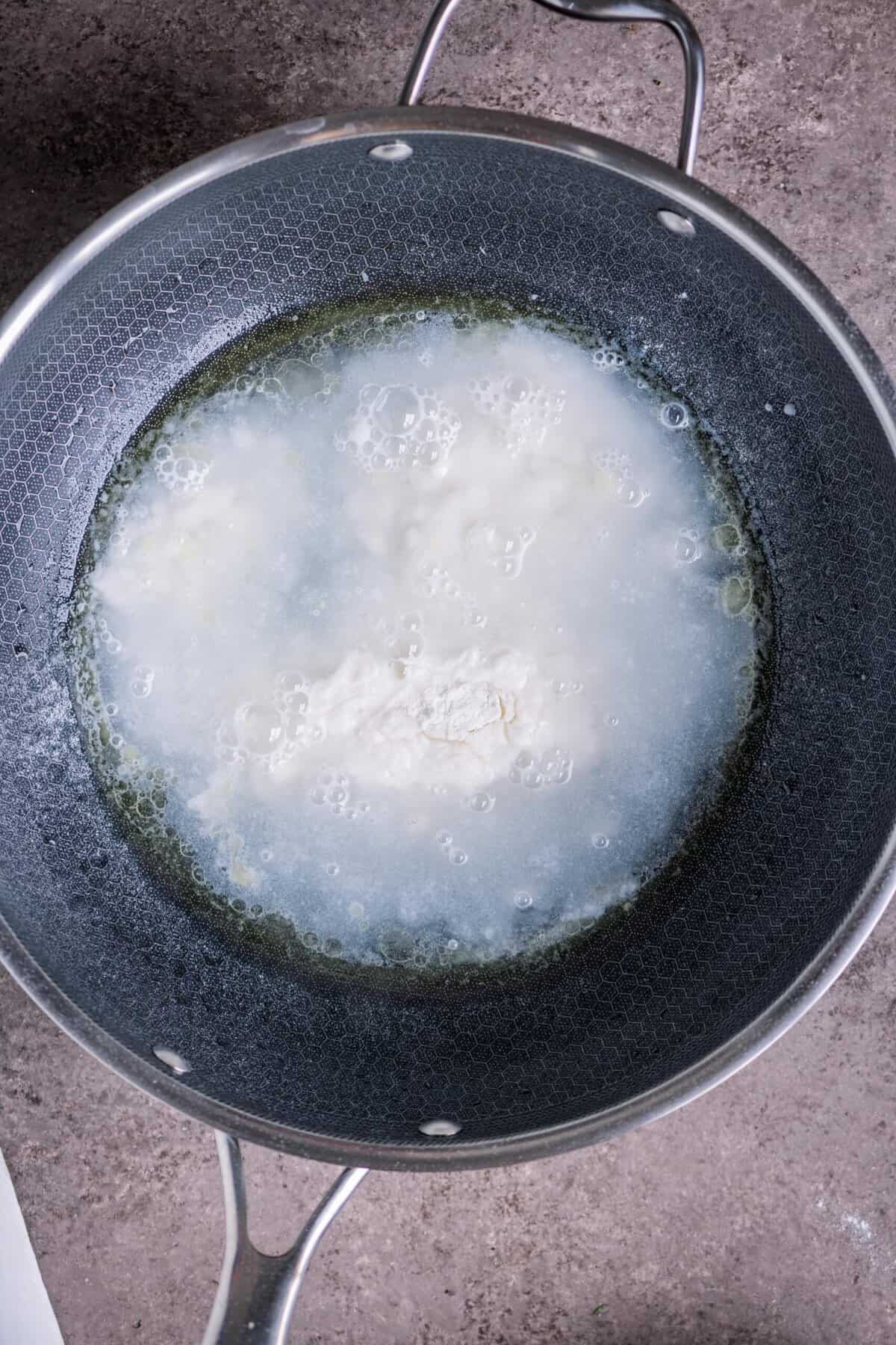 Rice flour being stirred into boiling water in a pan.