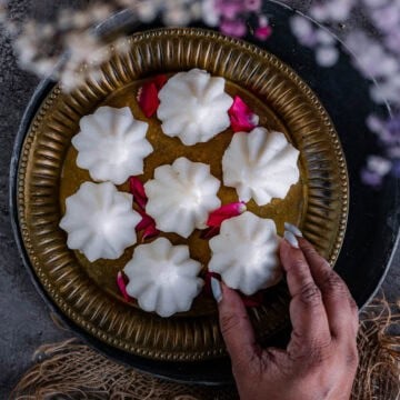 A hand picking up one kozhukattai from a plate.