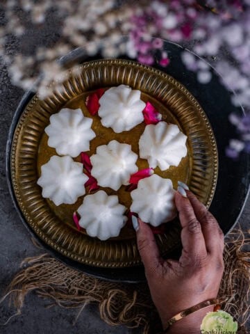 A hand picking up one kozhukattai from a plate.