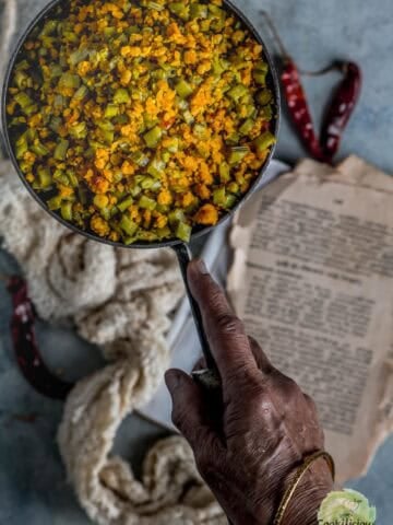 A hand holding a pan filled with Kothavarangai Paruppu Usili.