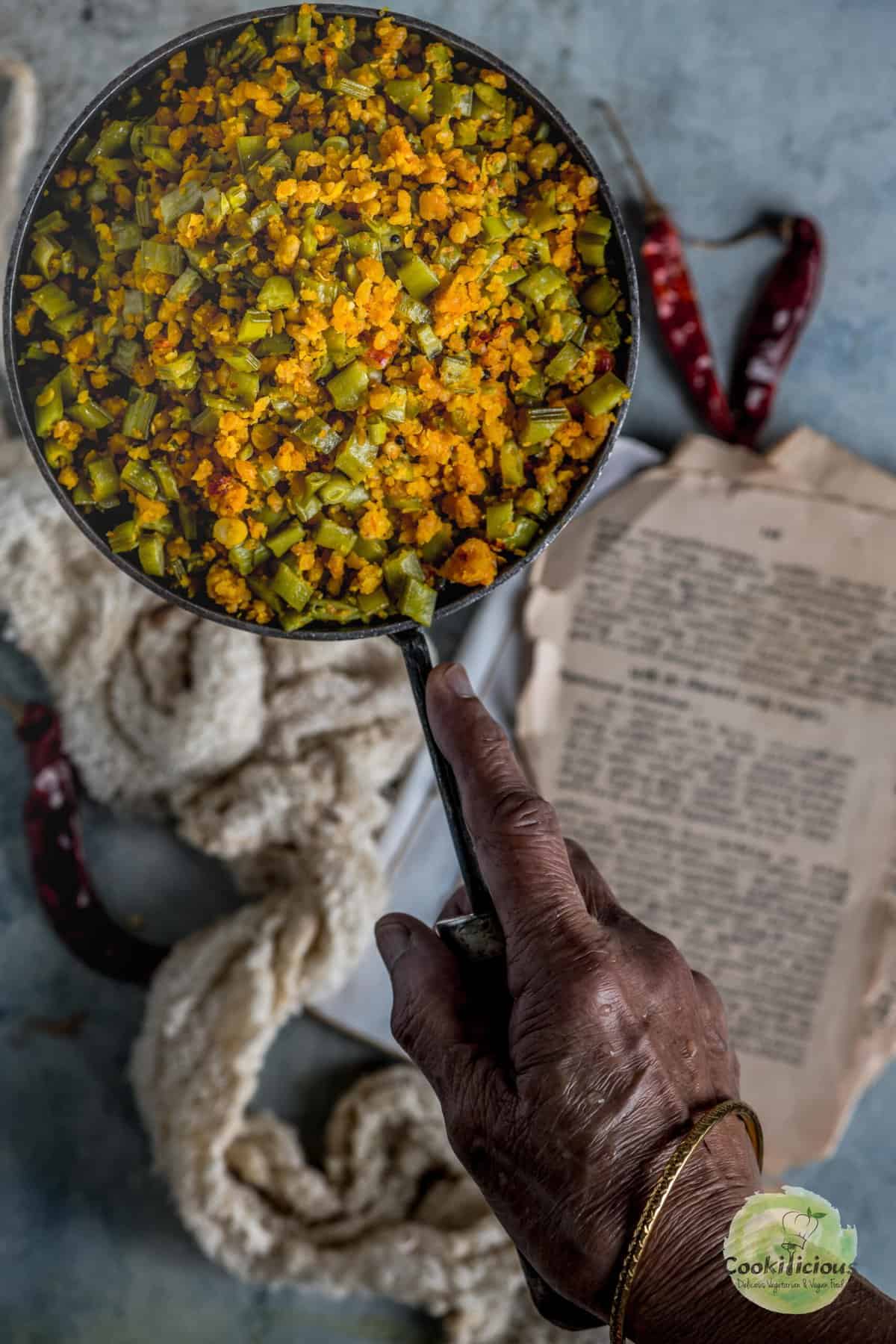 A hand holding a pan filled with Kothavarangai Paruppu Usili.