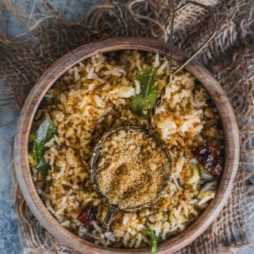 a bowl of sesame rice served with a small bowl filled with ellu podi in the middle.