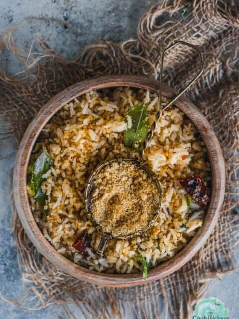 a bowl of sesame rice served with a small bowl filled with ellu podi in the middle.