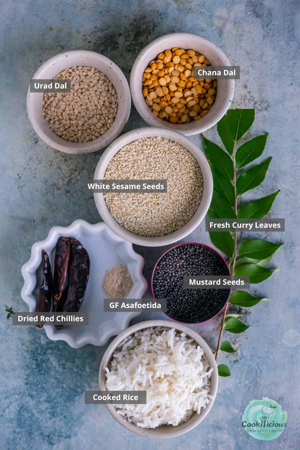 Ingredients for Ellu Podi Sadam including roasted sesame seeds, lentils, spices, and cooked rice arranged on a table with labels on them.