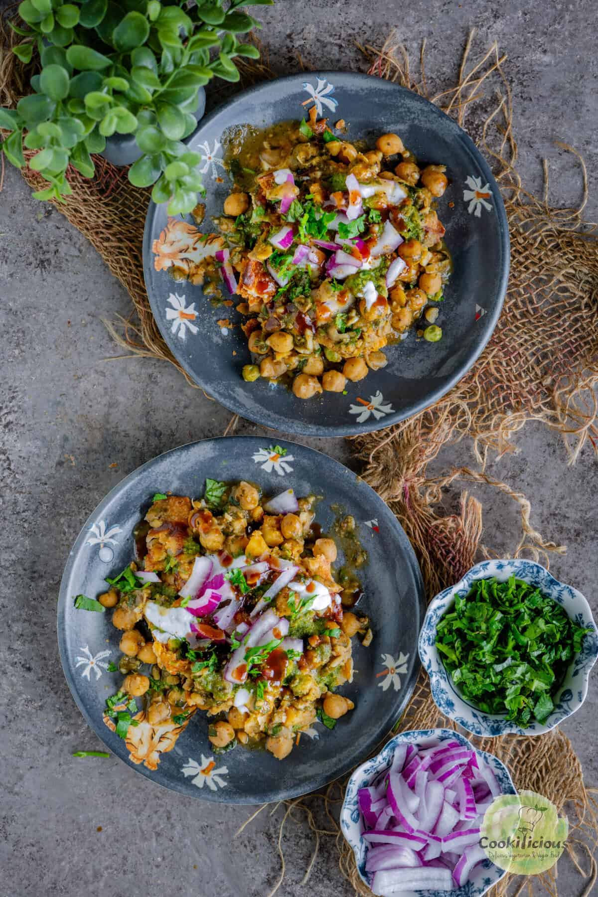 Street-style samosa chaat served in two small plates with crispy samosas, chickpea curry, chutneys, yogurt, sev, and fresh cilantro garnish.