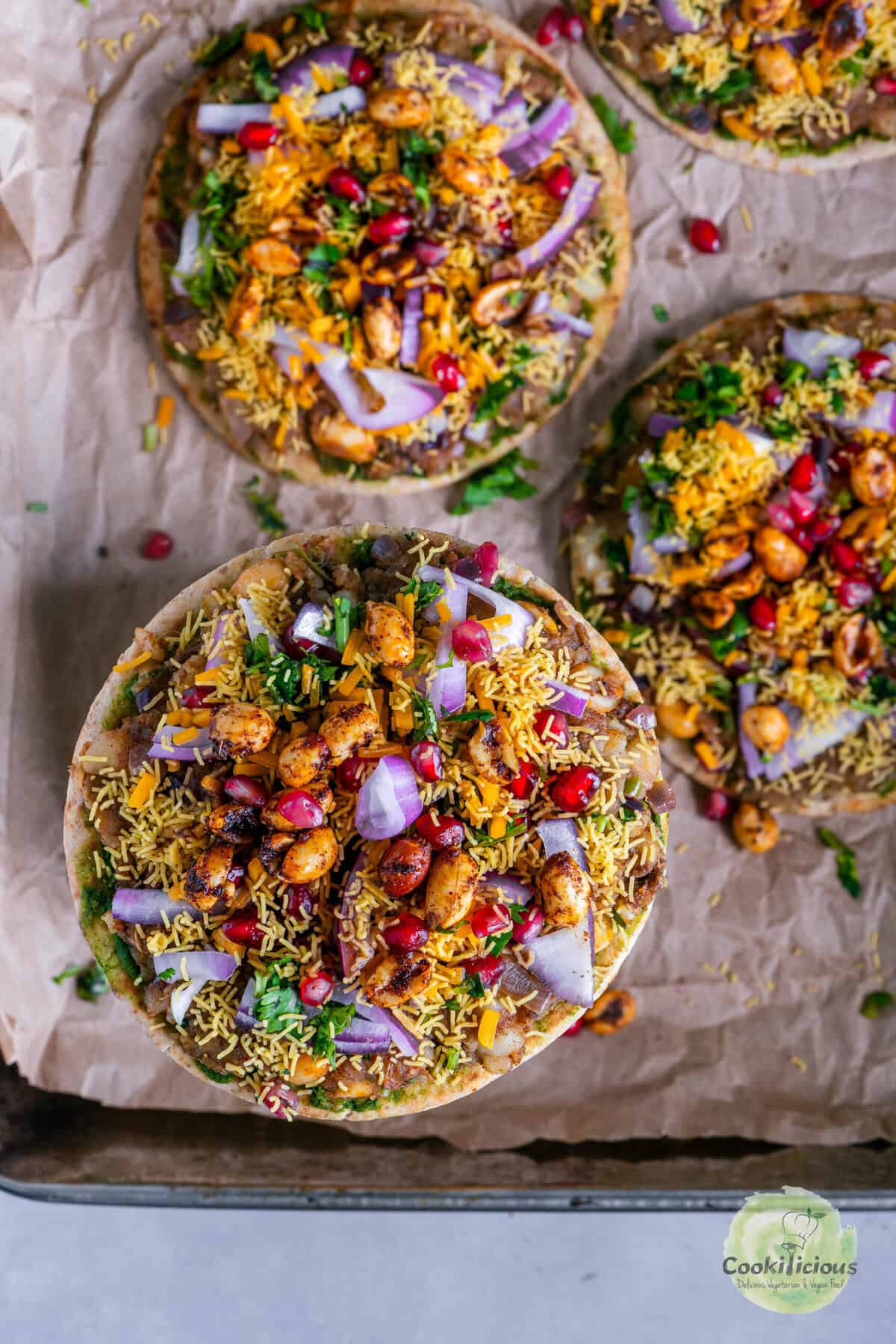 Cheesy Dabeli Pizza on mini pita bread with dabeli masala, pomegranate seeds, spiced peanuts, and crispy sev – easy Indian street food fusion snack.
