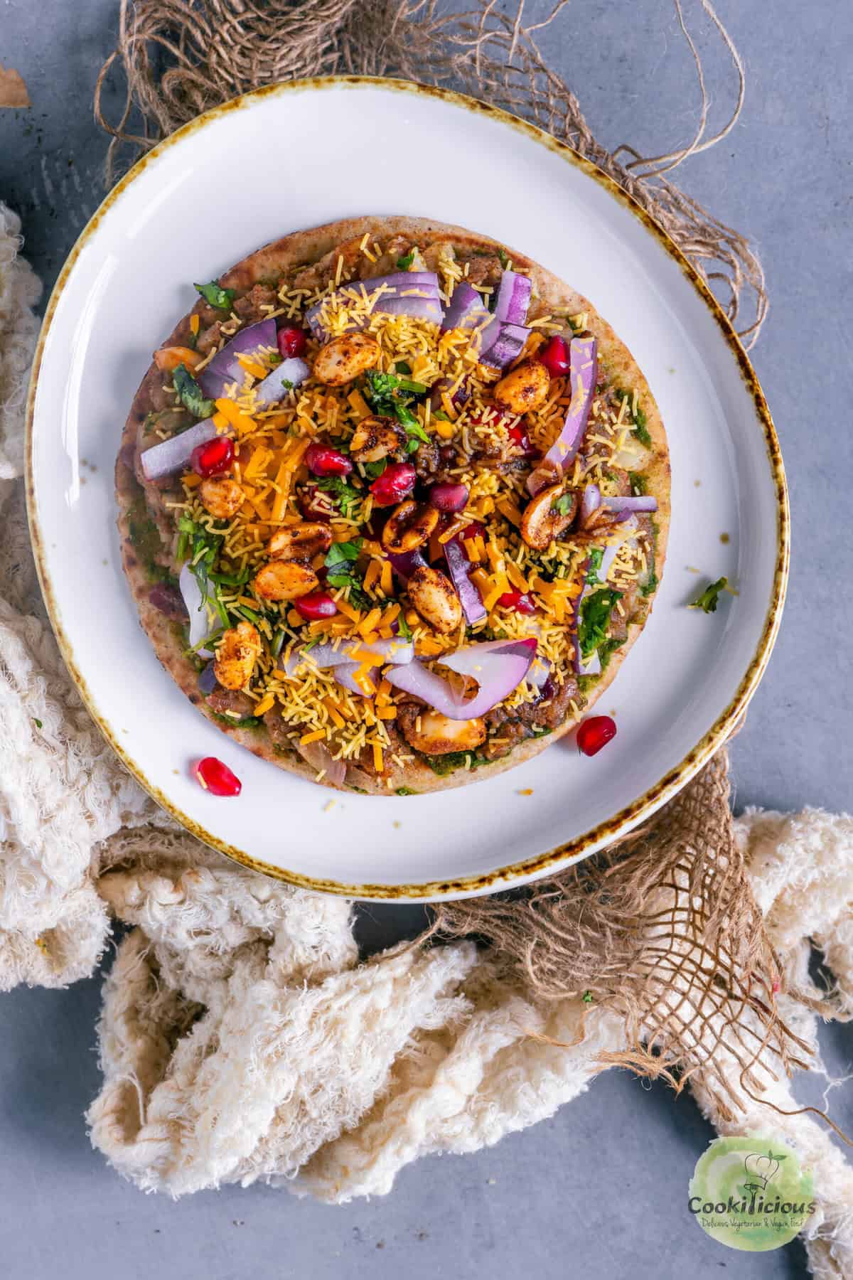 Vegan Dabeli Pizza topped with dabeli masala, sev, spiced peanuts, pomegranate, and melted cheese on mini pita bread, perfect Indian fusion snack.