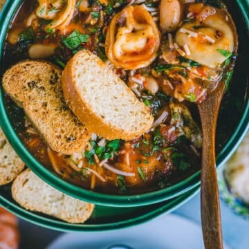 Bowl of vegan tortellini soup served with crusty bread and a sprinkle of basil.