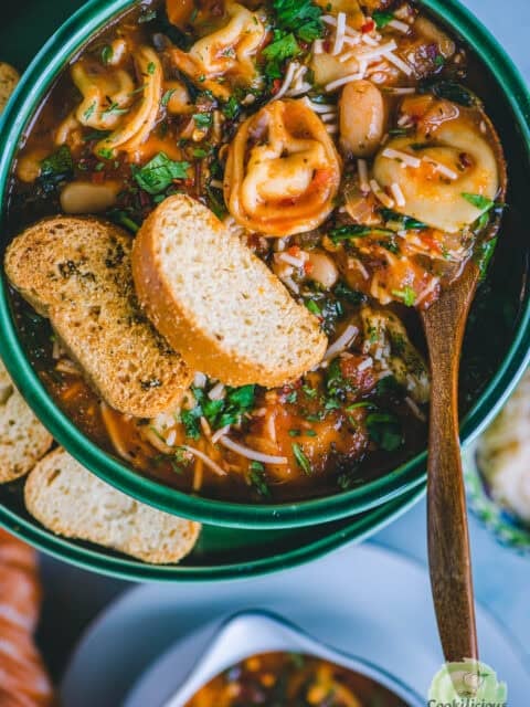 Bowl of vegan tortellini soup served with crusty bread and a sprinkle of basil.