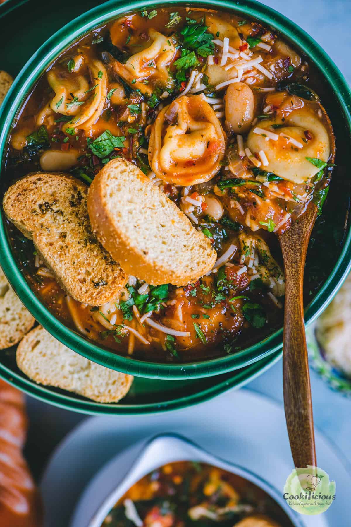 Bowl of vegan tortellini soup served with crusty bread and a sprinkle of basil.