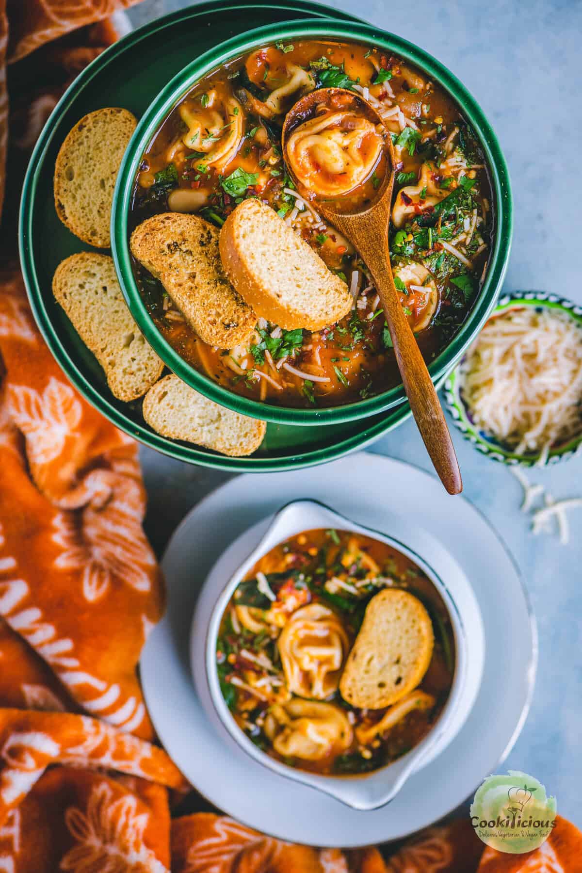 Creamy tomato-based vegan tortellini soup in a green bowl with bread on a rustic table.