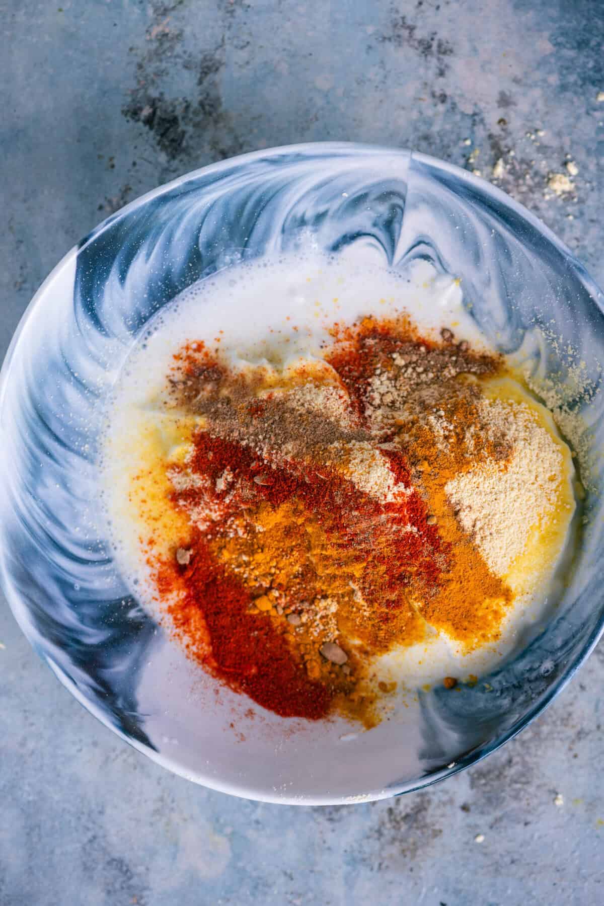 Sprinkling red chili powder, turmeric powder, and amchur (dry mango) powder into the yogurt.
